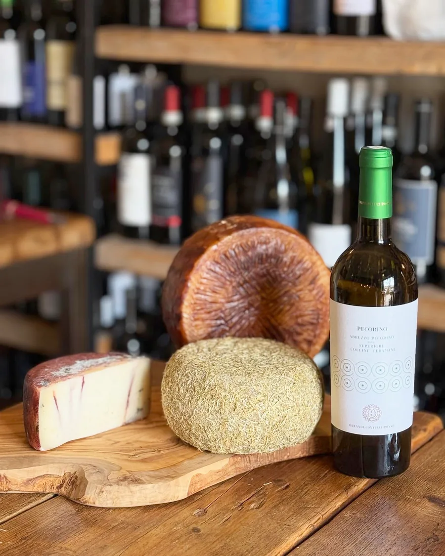 Tagliere di pecorini e formaggi selezionati accanto a una bottiglia di vino bianco