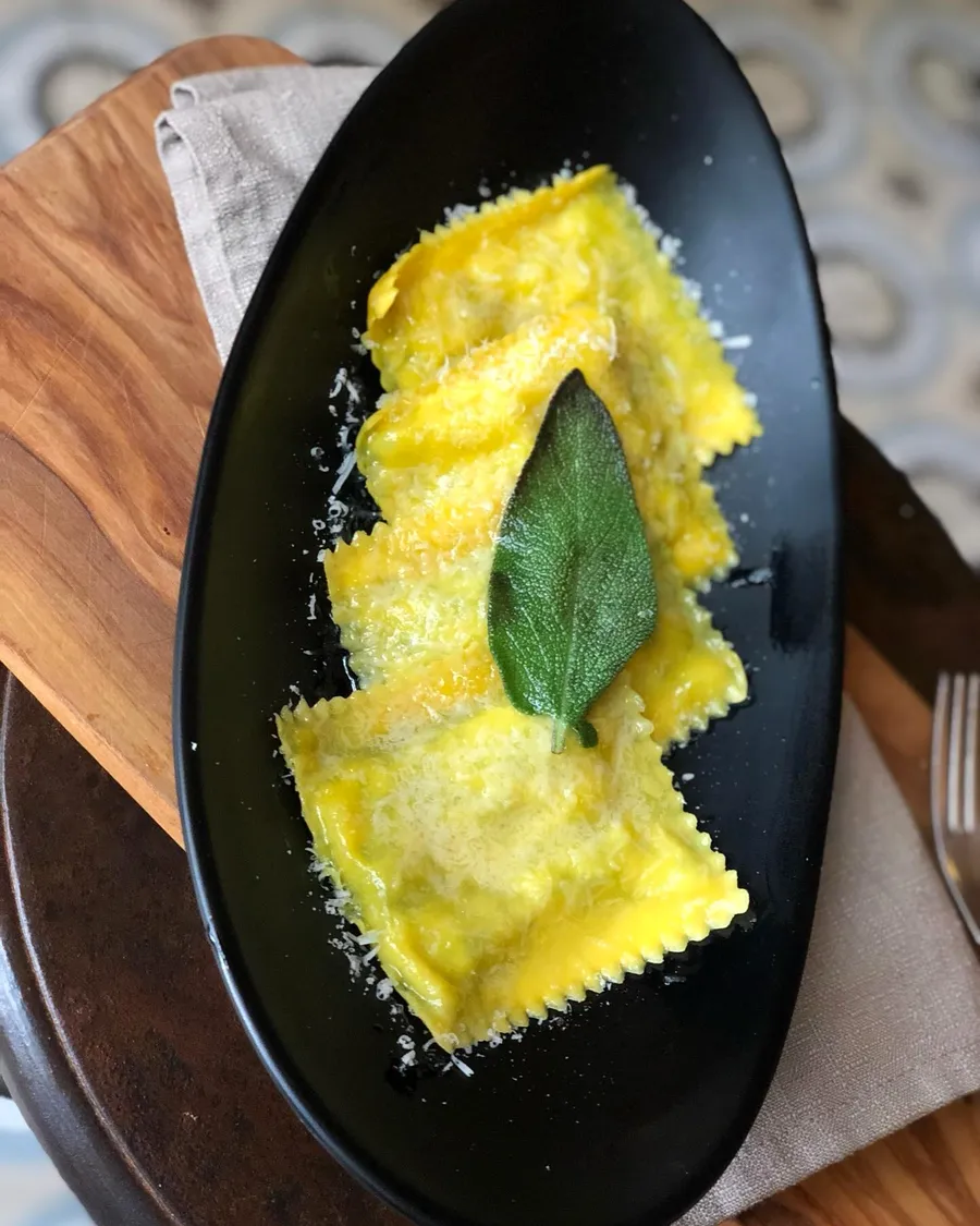 Ravioli ripieni di ricotta e spinaci con burro e salvia, su piatto scuro
