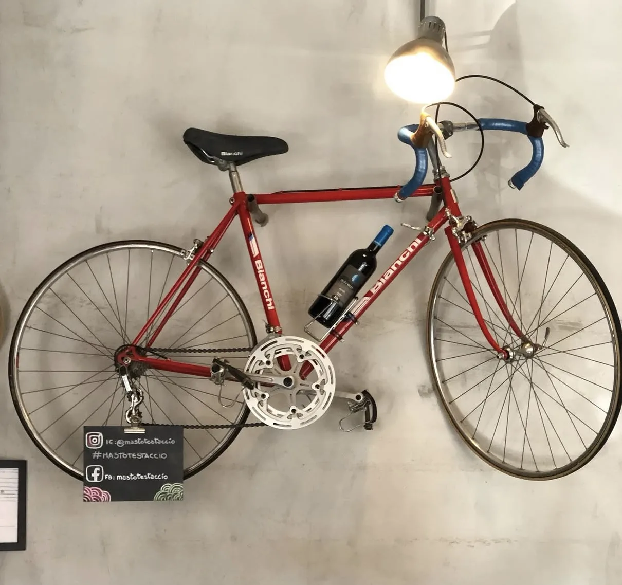 Una Bianchi rossa vintage appesa in sala, accanto a una bottiglia di vino