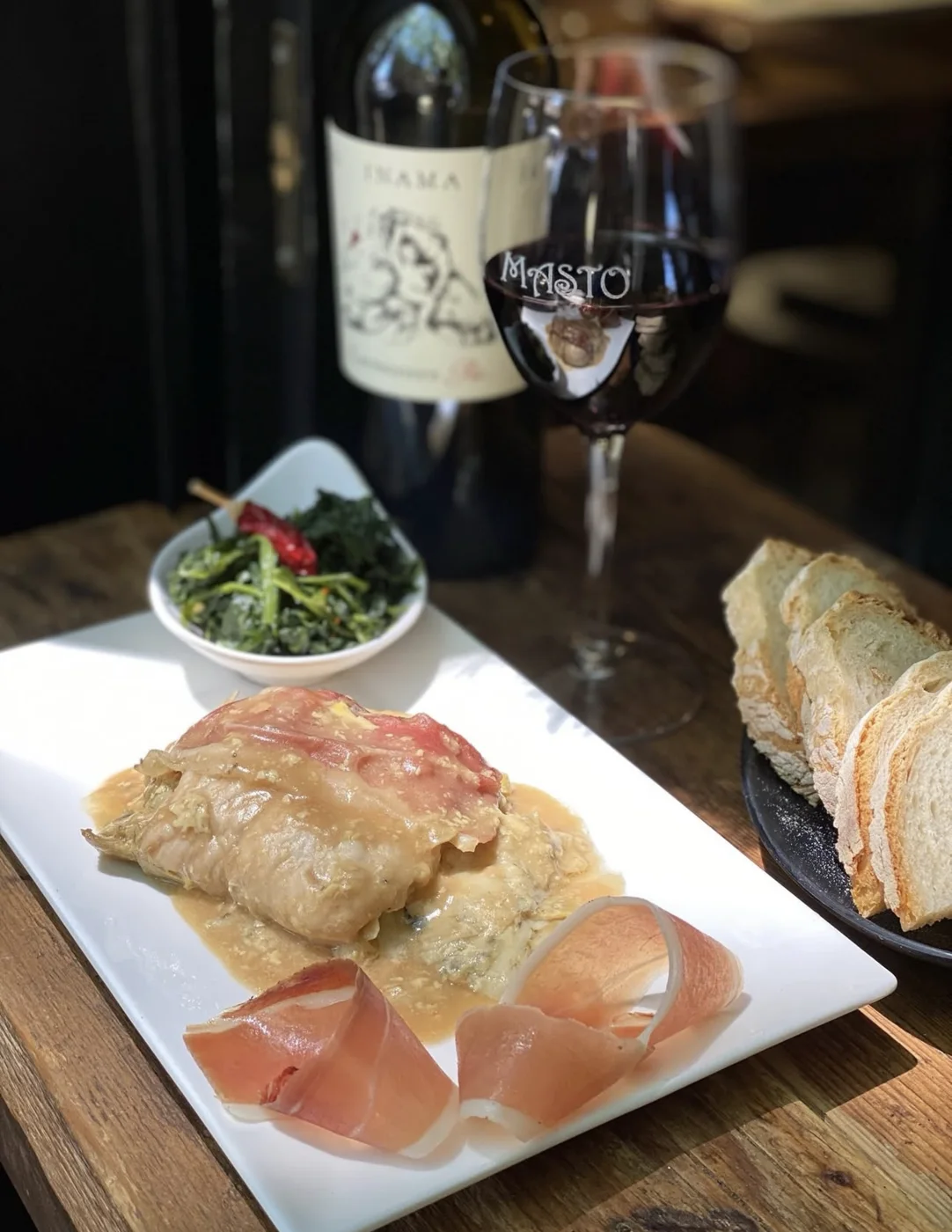 Un piatto con riccioli di crudo, pane e il calice MASTO, in controluce