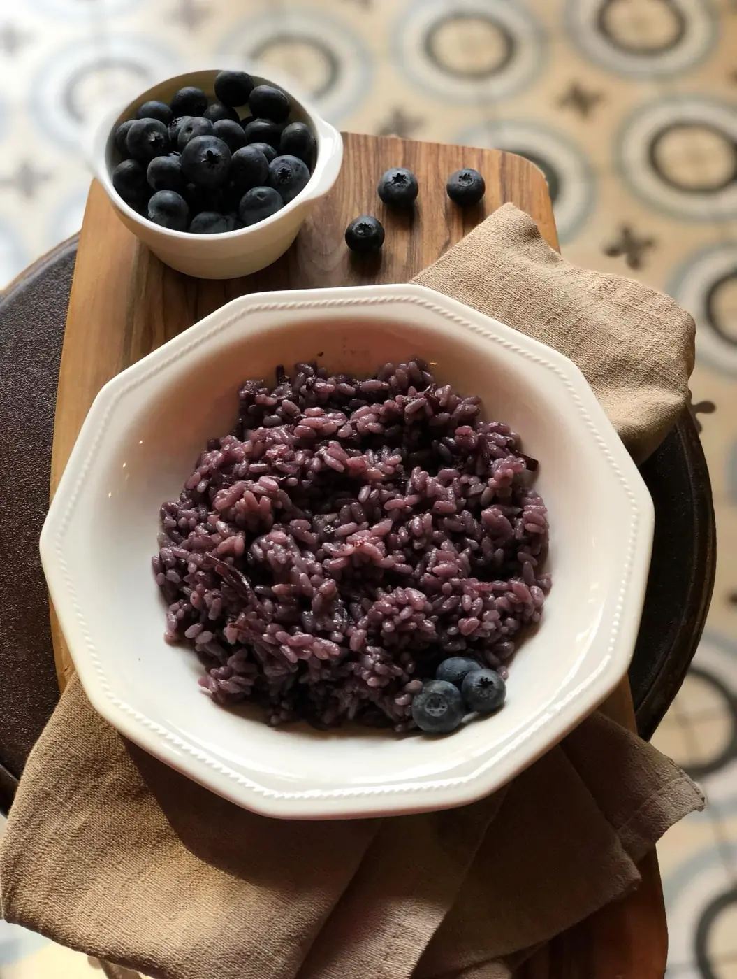 Risotto ai mirtilli con fonduta, servito in una scodella bianca su un tagliere di legno