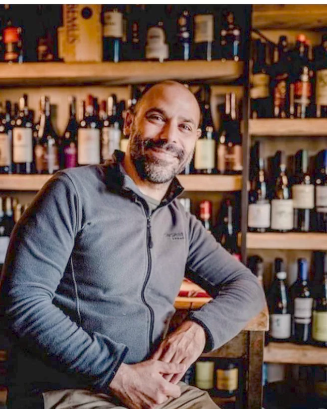 Emiliano seduto davanti alla parete dei vini dell'enoteca